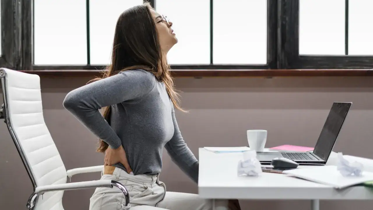 Femme assise à un bureau, se tenant le bas du dos, souffrant d'une mauvaise posture.