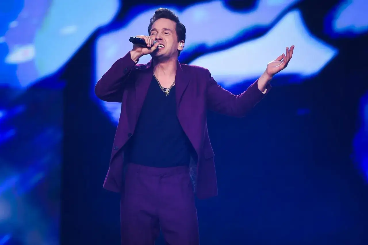 Artysta w bordowym garniturze śpiewa na scenie podczas MTV Unplugged Polska, z ręką uniesioną w geście.