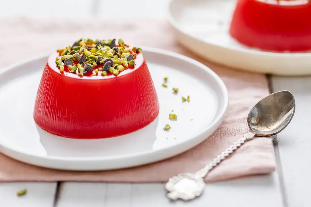 Delizioso gelo di melone rosso, guarnito con pistacchi tritati e gocce di cioccolato, pronto per essere gustato con un cucchiaino d'argento.
