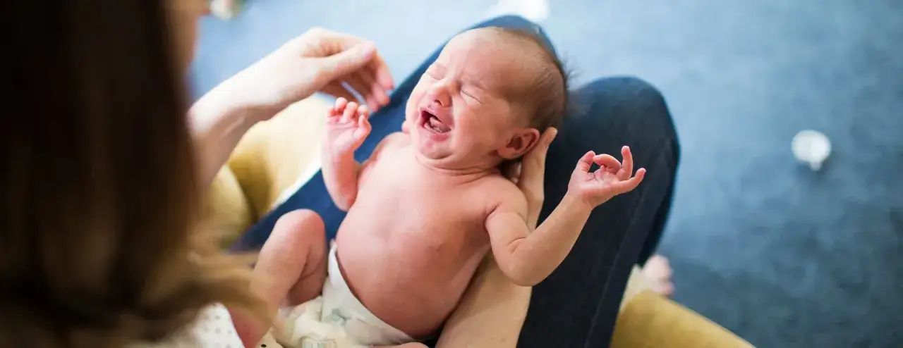 Ein weinendes Baby auf dem Schoß einer Person. Die Eltern sorgen sich um mögliche RSV-Symptome.
