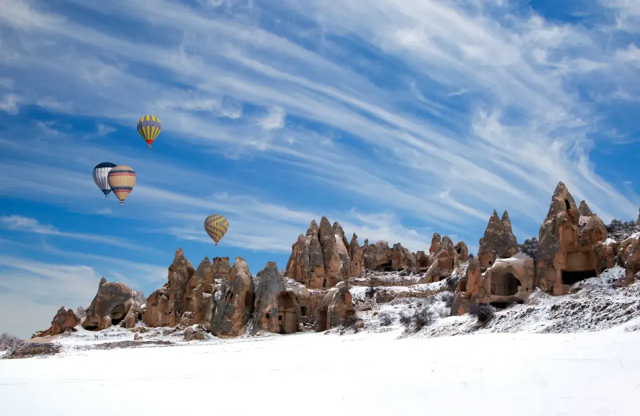 Balony unoszą się nad ośnieżonymi formacjami skalnymi w Kapadocji. Czy w Turcji pada śnieg? Tak, zimą krajobraz ten wygląda magicznie.