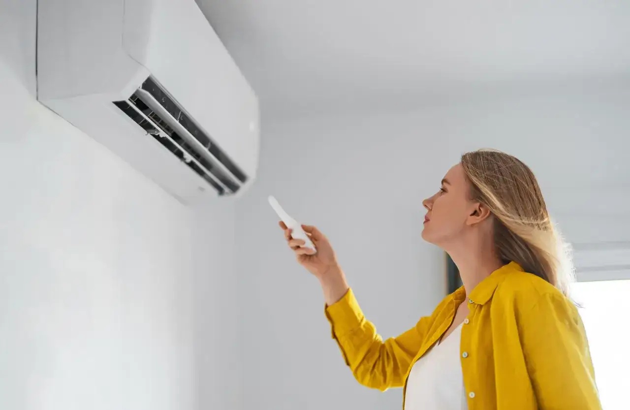 Mujer ajusta el aire acondicionado a la temperatura ideal para ahorrar energía.