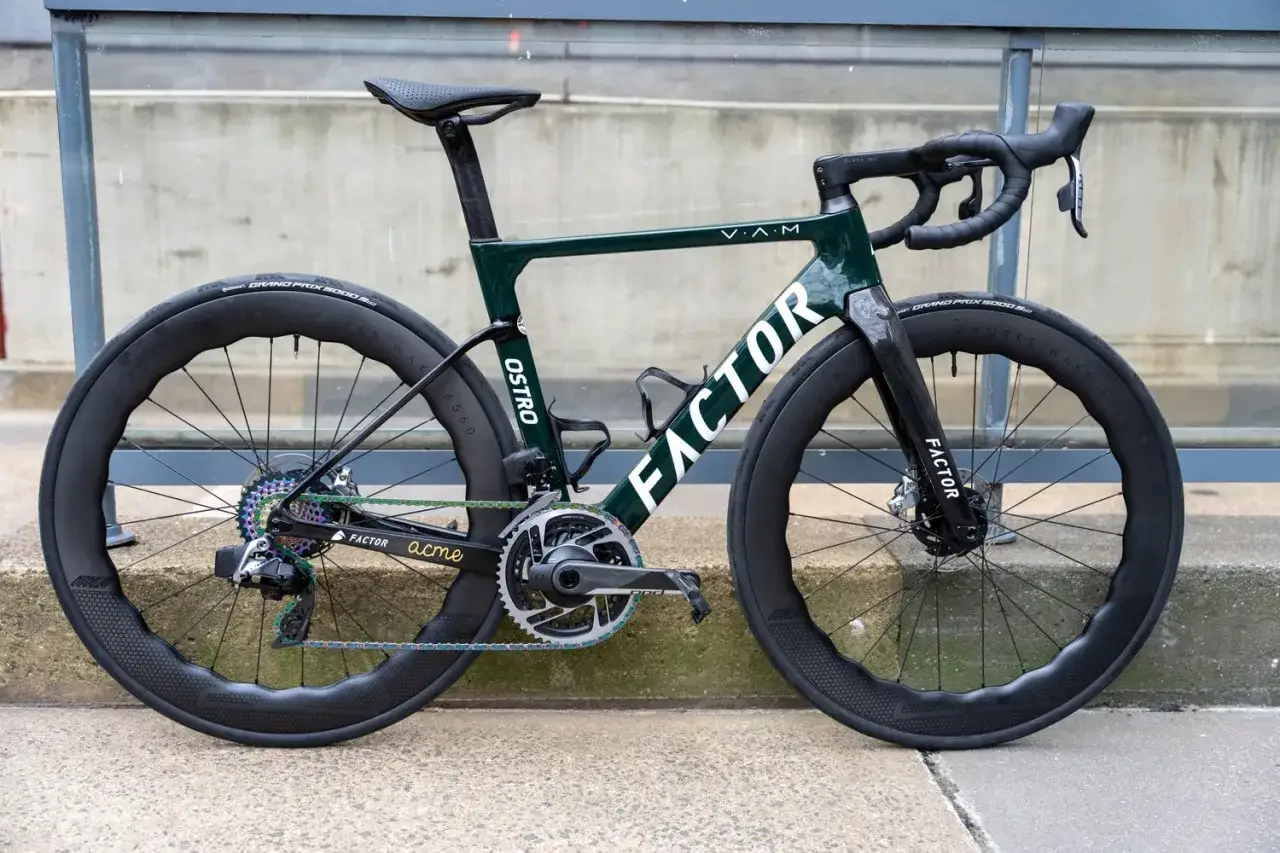 A sleek, dark green Factor Ostro road bike with deep-dish carbon wheels and a rainbow-colored chain, ready for a fast ride.