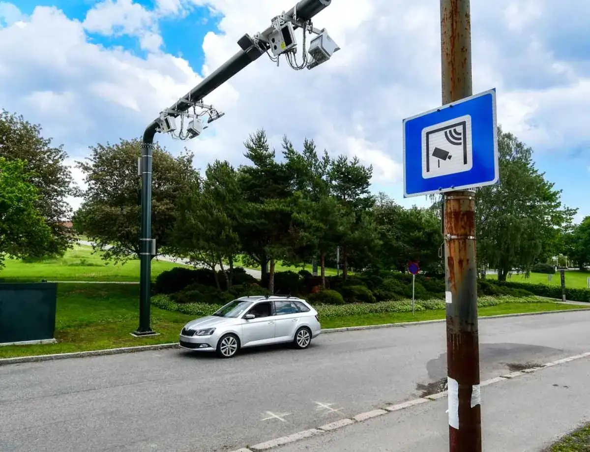 Silver svensk bil n&auml;rmar sig en autopass-portal i Norge. Skylt indikerar kamerabevakning.