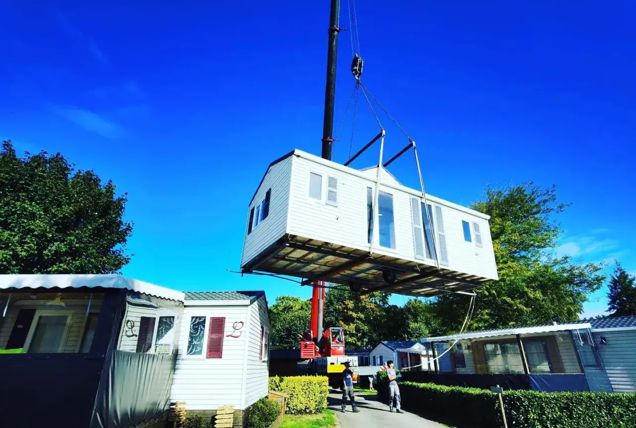 Une grue soul&egrave;ve un mobil home pour son installation. D'autres mobil homes sont visibles sur le site.