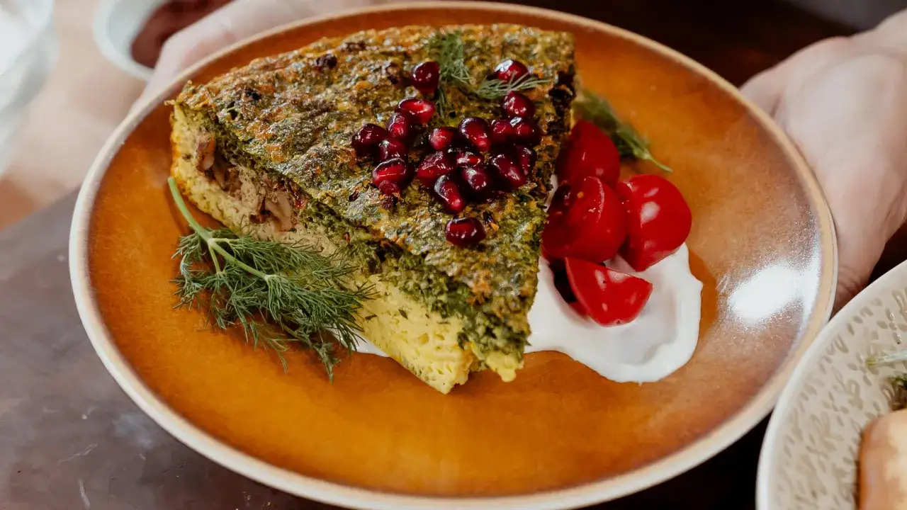 Tranche de kuku sabzi, un plat persan aux herbes, garnie de grenades et servie avec des tomates cerises et de la cr&egrave;me.