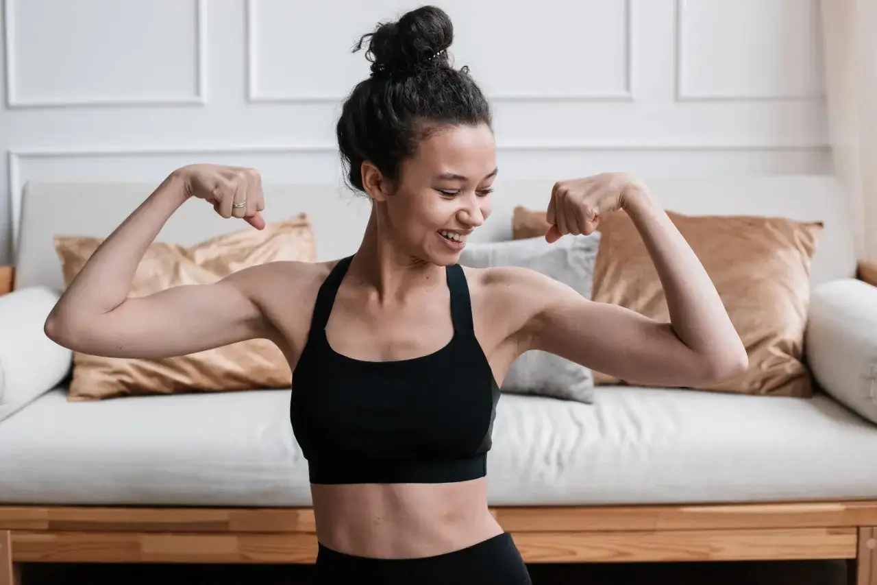 Mujer sonriente mostrando sus b&iacute;ceps, un ejemplo de cu&aacute;les son los ejercicios de fuerza.