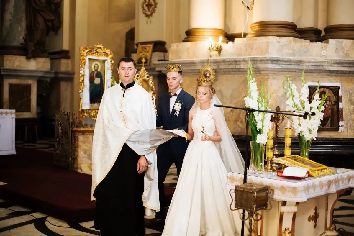 Przebieg ślubu kościelnego: ksiądz, pan młody i panna młoda w koronach, podczas ceremonii w kościele.