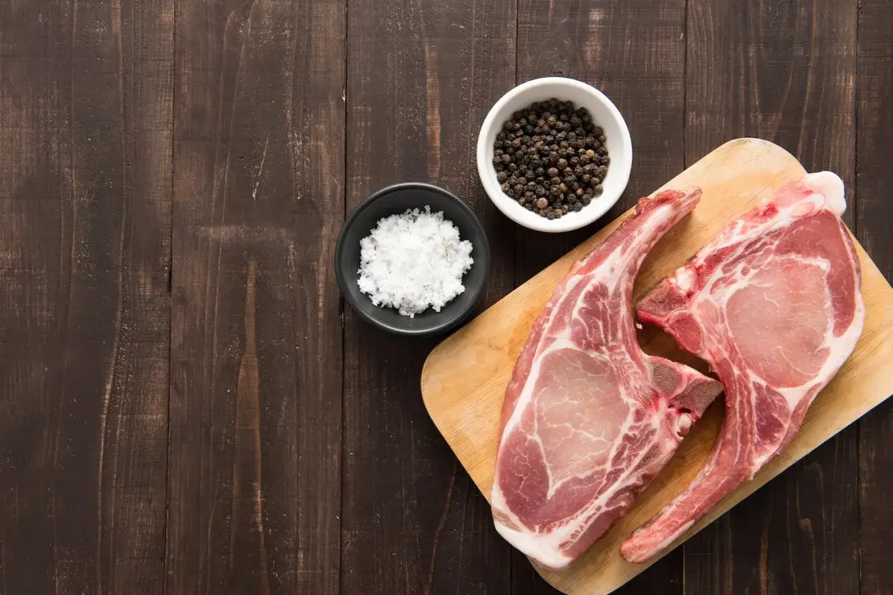 Deux belles c&ocirc;tes de porc crues, pr&ecirc;tes &agrave; &ecirc;tre assaisonn&eacute;es avec du sel et du poivre noir en grains.