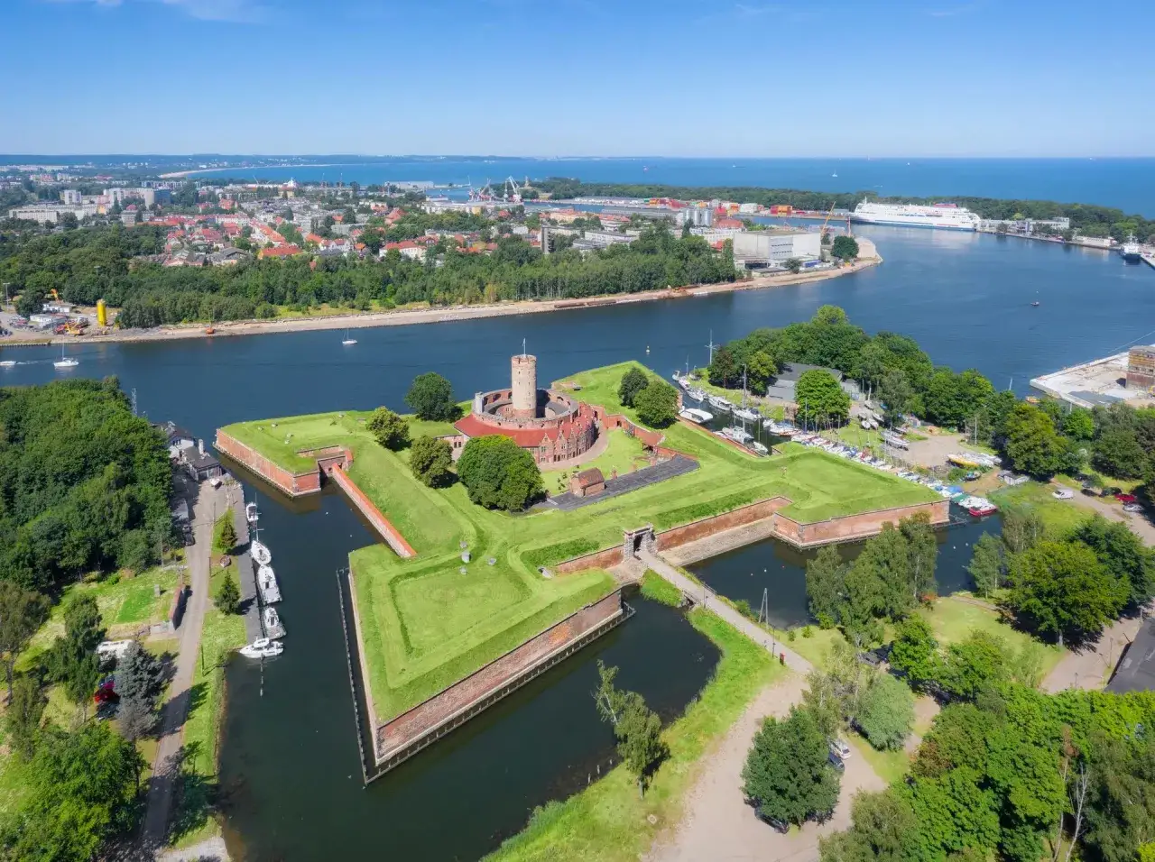 Twierdza Wisłoujście z lotu ptaka, otoczona fosą, z widokiem na port i morze.