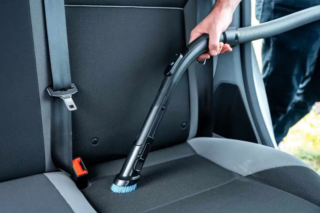 Un hombre aspira los asientos del coche, mostrando c&oacute;mo limpiar los asientos del coche para un interior impecable.