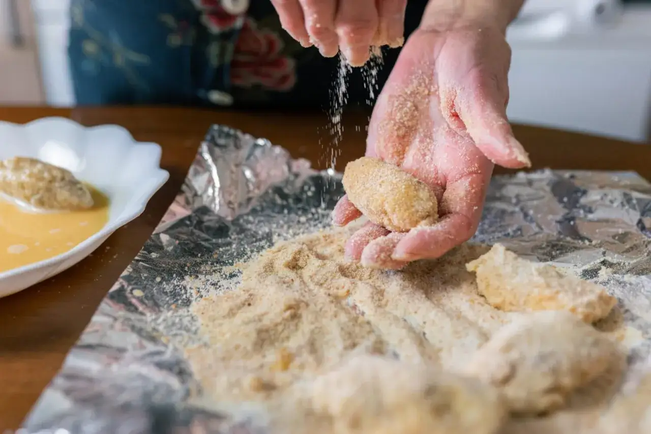 Manos cubriendo croquetas con pan rallado. La proporción de harina y leche para croquetas es clave para su textura.