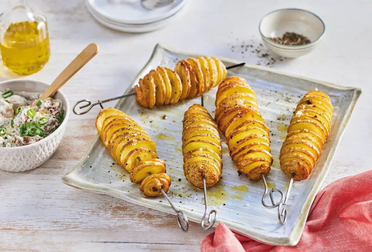Spiral kartoffelgerichte auf Spießen, goldbraun gebacken, mit Dip und Öl daneben.