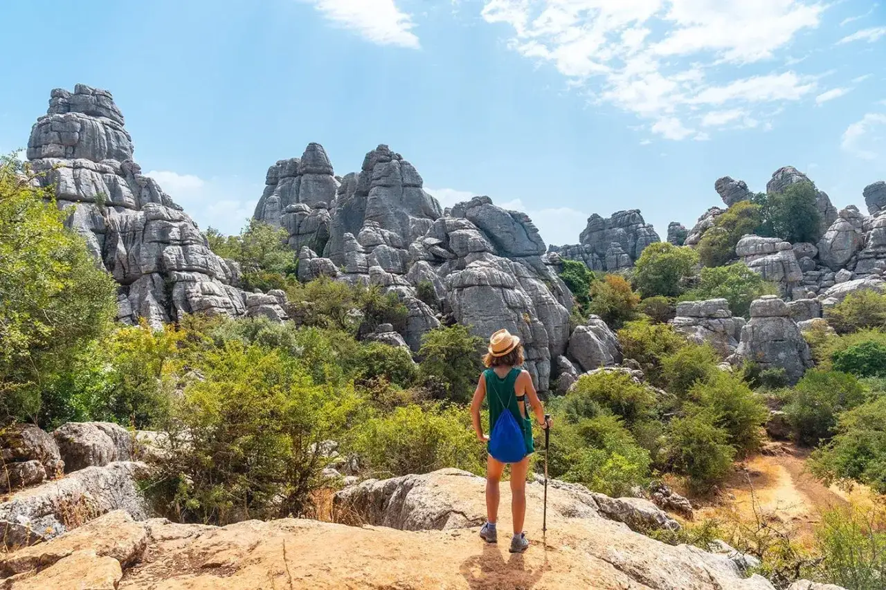 Une randonneuse admire un paysage rocheux spectaculaire lors d'un trek en Espagne. Le soleil brille sur les formations calcaires et la v&eacute;g&eacute;tation luxuriante.