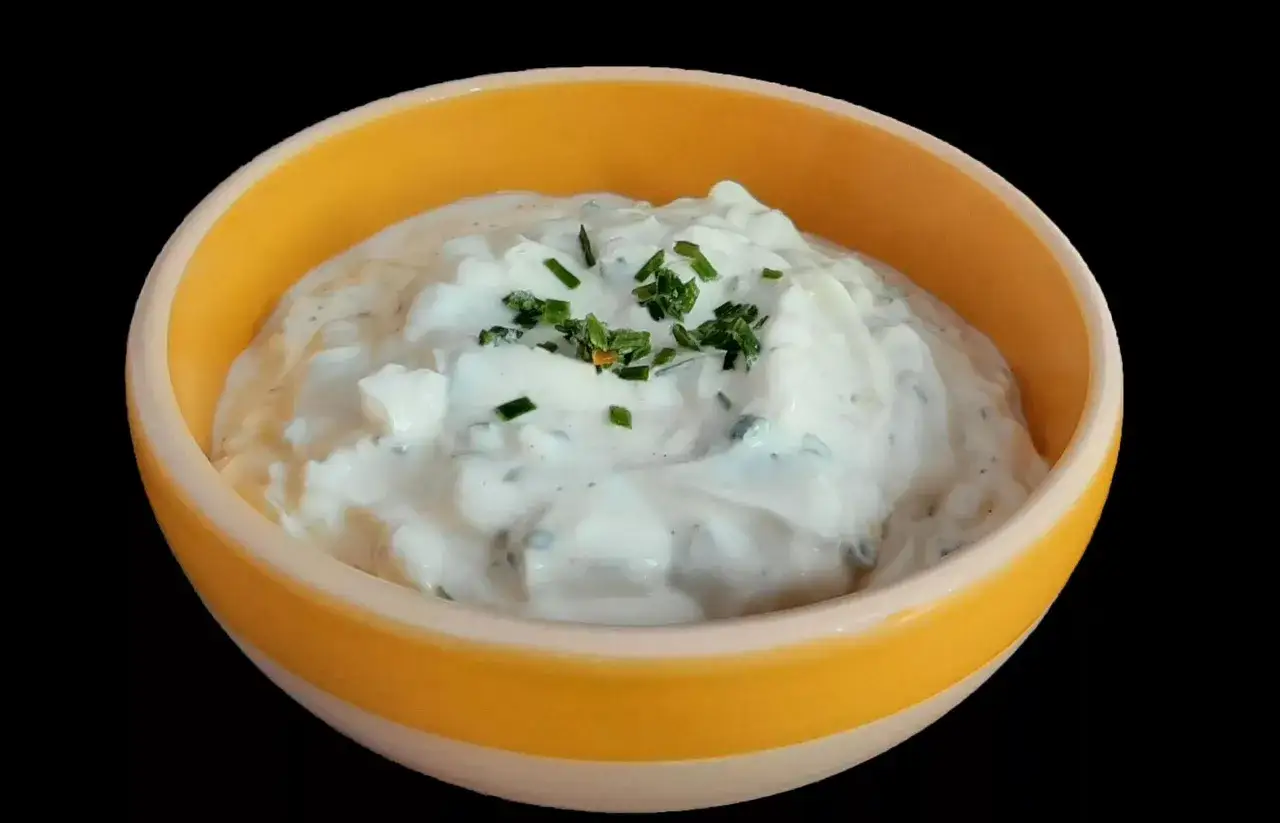 Sauce onctueuse à base de fromage blanc et ciboulette fraîche, garnie de brins d'herbe verte, servie dans un bol jaune vif.