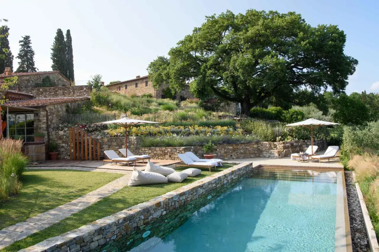 Piscine et salon de jardin dans une r&eacute;sidence toscane avec vue sur les collines et un grand ch&ecirc;ne.