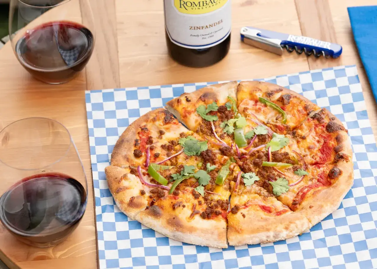 Une pizza chorizo appétissante, garnie de poivrons verts et d'oignons rouges, est prête à être dégustée avec un verre de vin rouge.