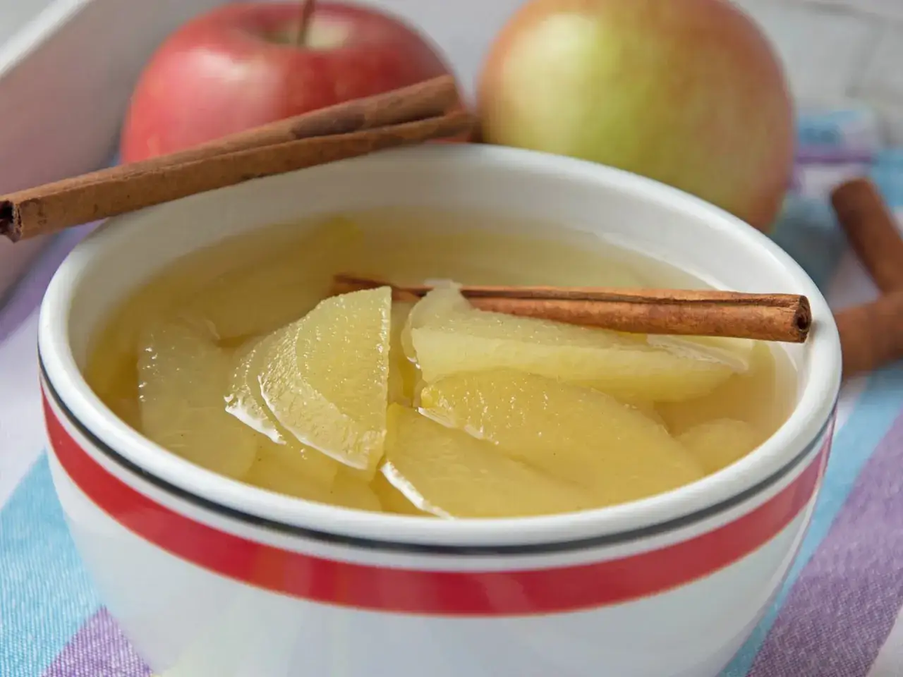 Schon probiert, Apfelkompott selber machen? Hier ist ein köstliches Ergebnis: weiche Apfelstücke in Sirup mit Zimtstangen, garniert mit frischen Äpfeln.