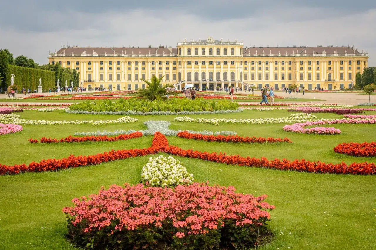 Schloss Schönbrunn mit blühenden Blumenbeeten. Die Farbenpracht deutet auf die wien beste reisezeit im Frühling oder Sommer hin.