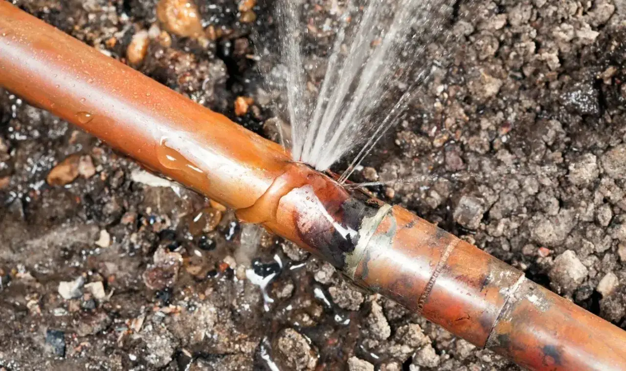 Gros plan sur un tuyau de cuivre percé, projetant de l'eau. Urgence : stop fuite eau !