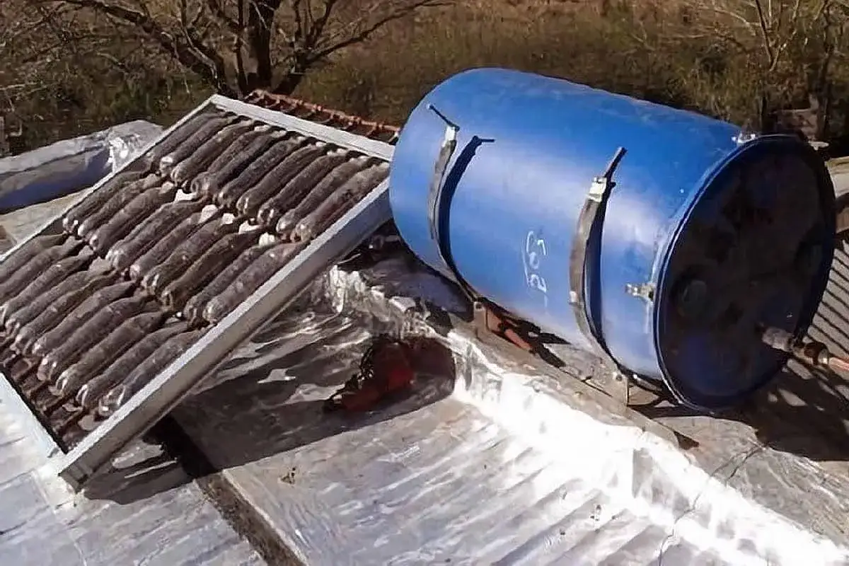 Un chauffe eau solaire fait maison sur un toit, avec un panneau collecteur et un réservoir bleu.