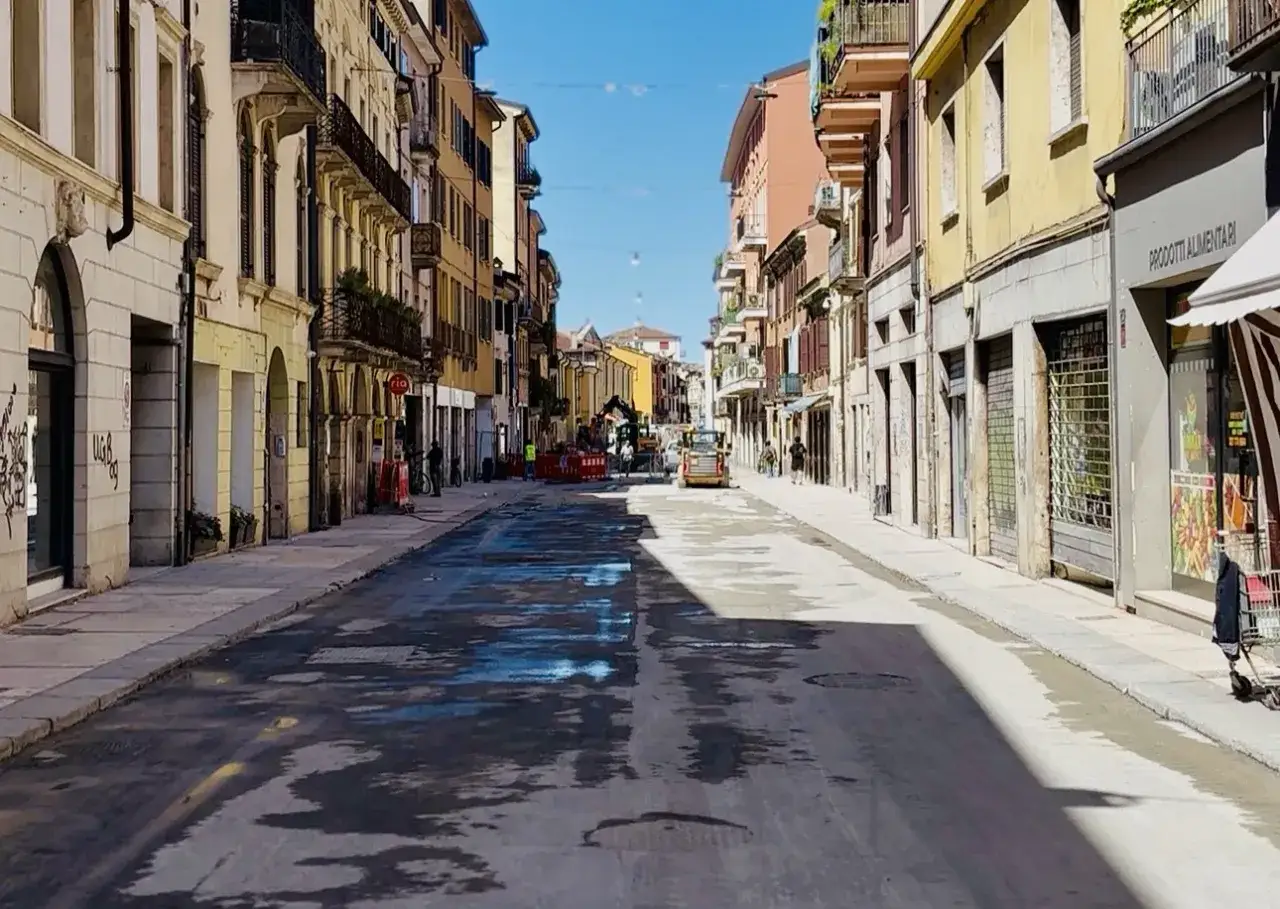 Strada a senso unico con cantieri in corso, macchine edili e palazzi colorati sotto un cielo azzurro.