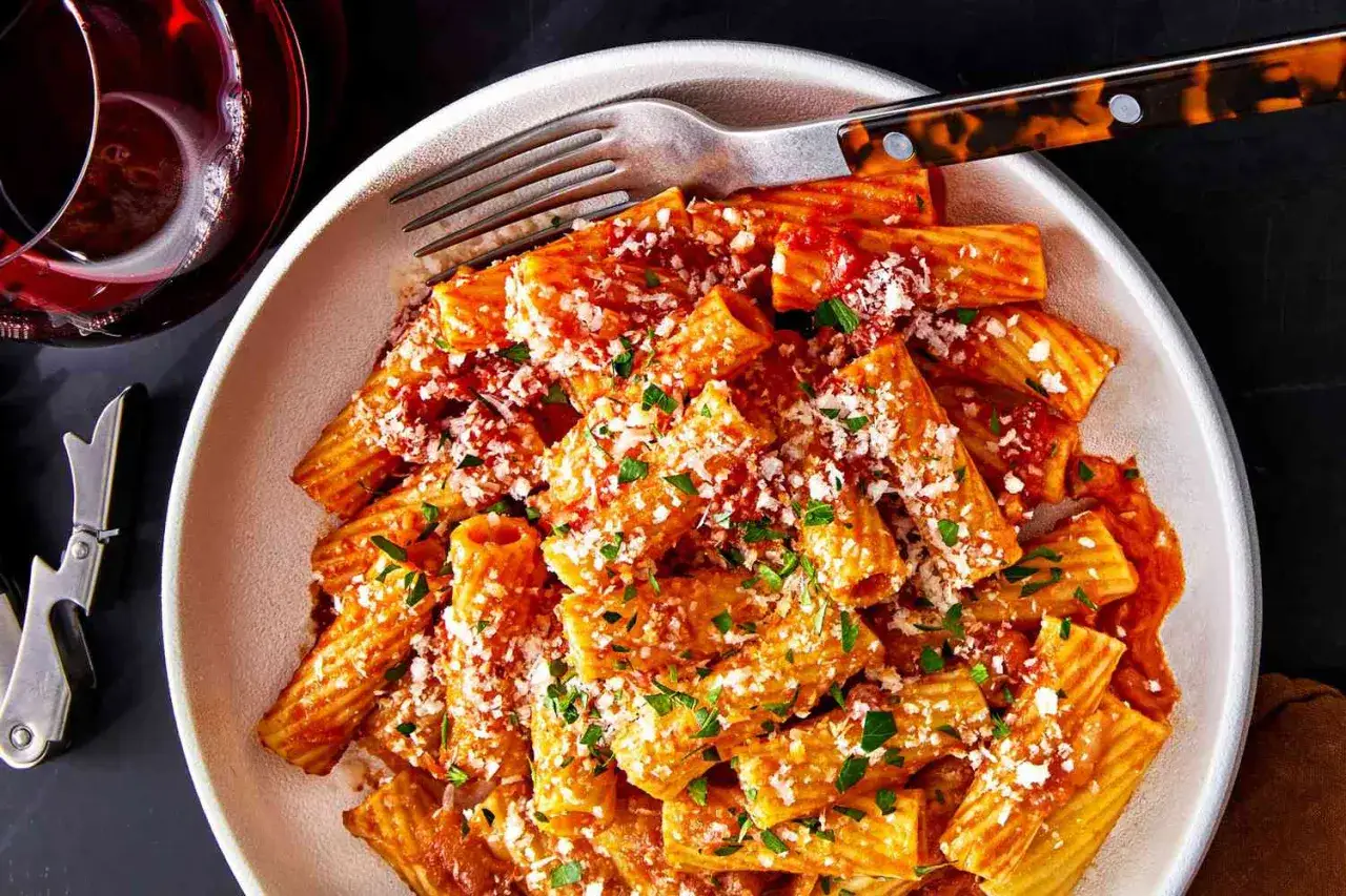 Un plat de rigatoni all'amatriciana, généreusement saupoudré de parmesan et de persil frais, prêt à être dégusté avec un verre de vin rouge.