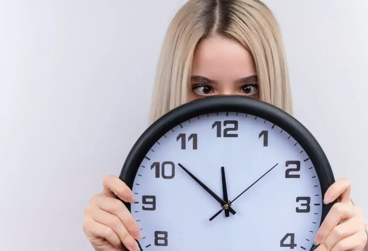 Dziewczyna z blond włosami ukrywa się za zegarem. Czyżby czas miał dla niej jakieś szczególne 2233 znaczenie?
