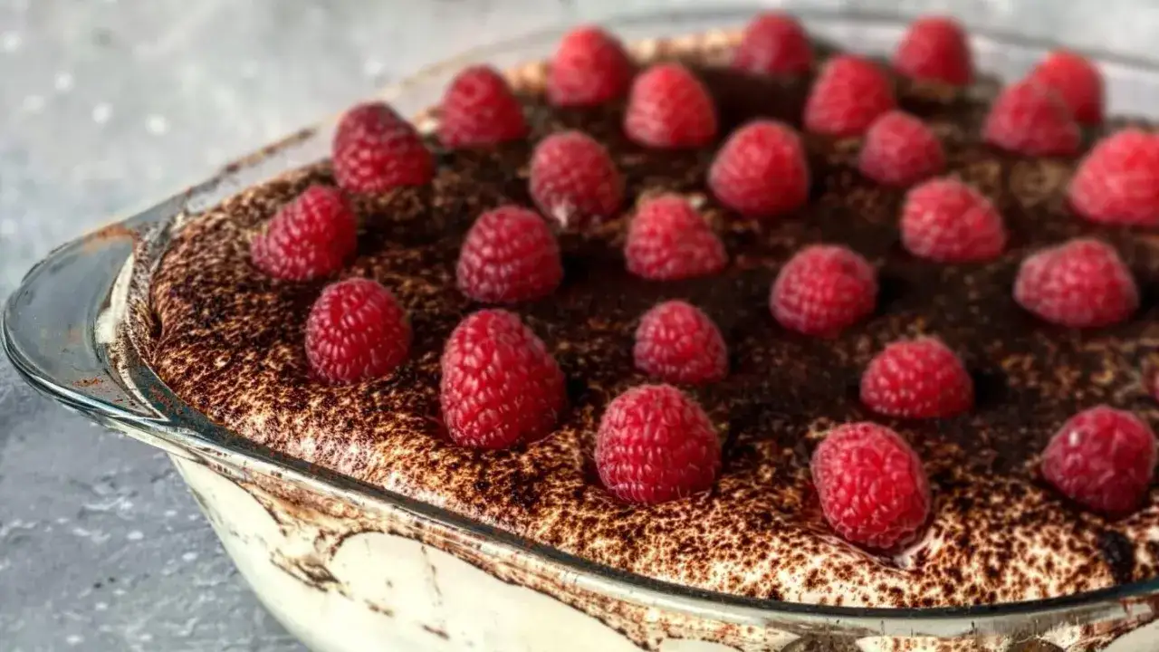 Pyszne tiramisu bez alkoholu, udekorowane malinami i posypane kakao, w szklanej formie.