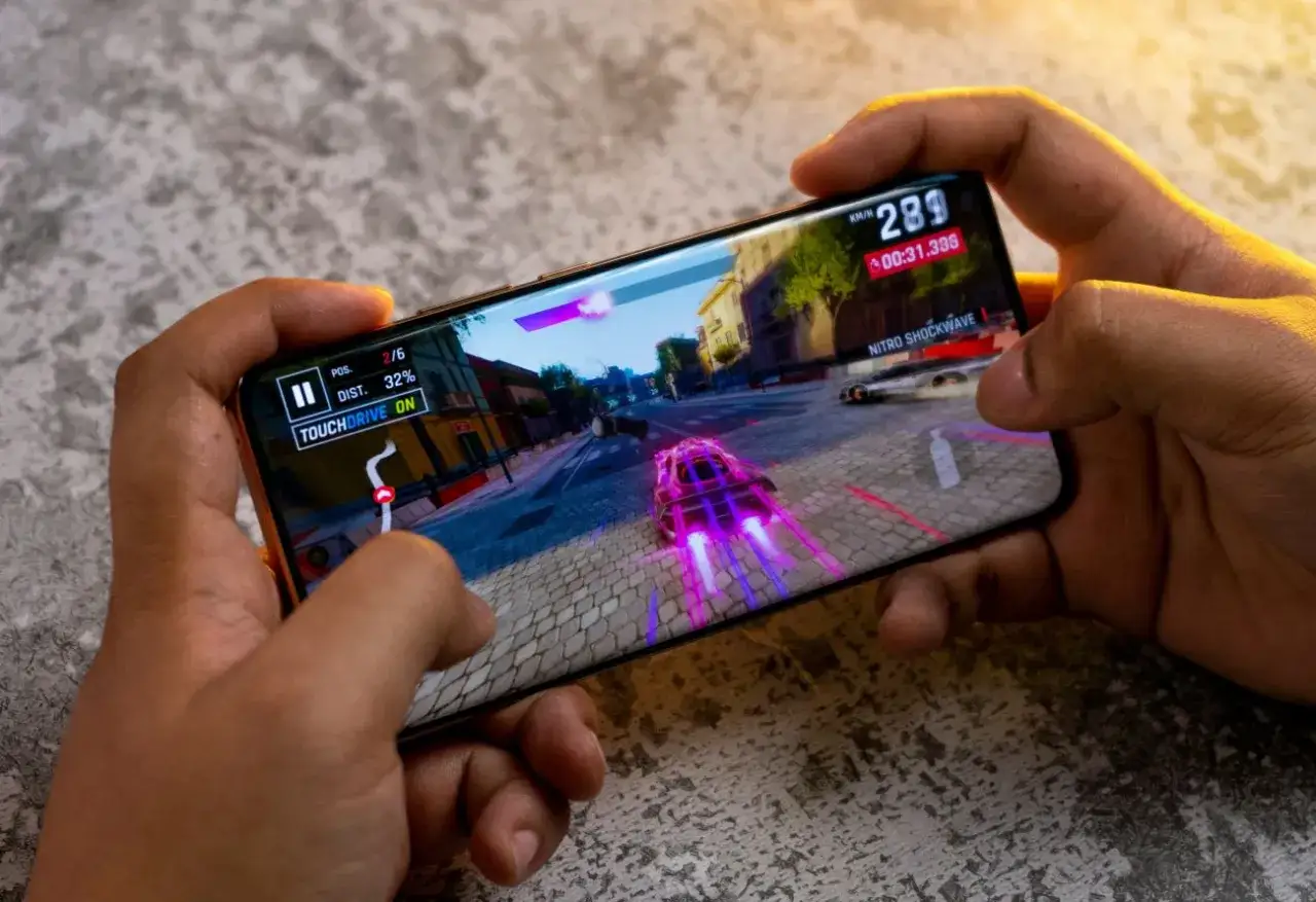 Ręce trzymają smartfon, na którym gra wyścigowa. Idealny telefon do 2500 zł poradzi sobie z taką grafiką.