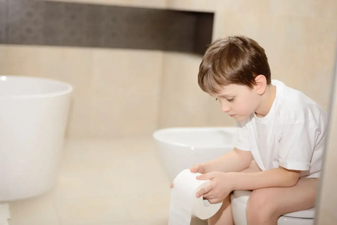Niño preocupado en el baño, con un rollo de papel, podría tener estreñimiento en niños de 5 a 10 años.