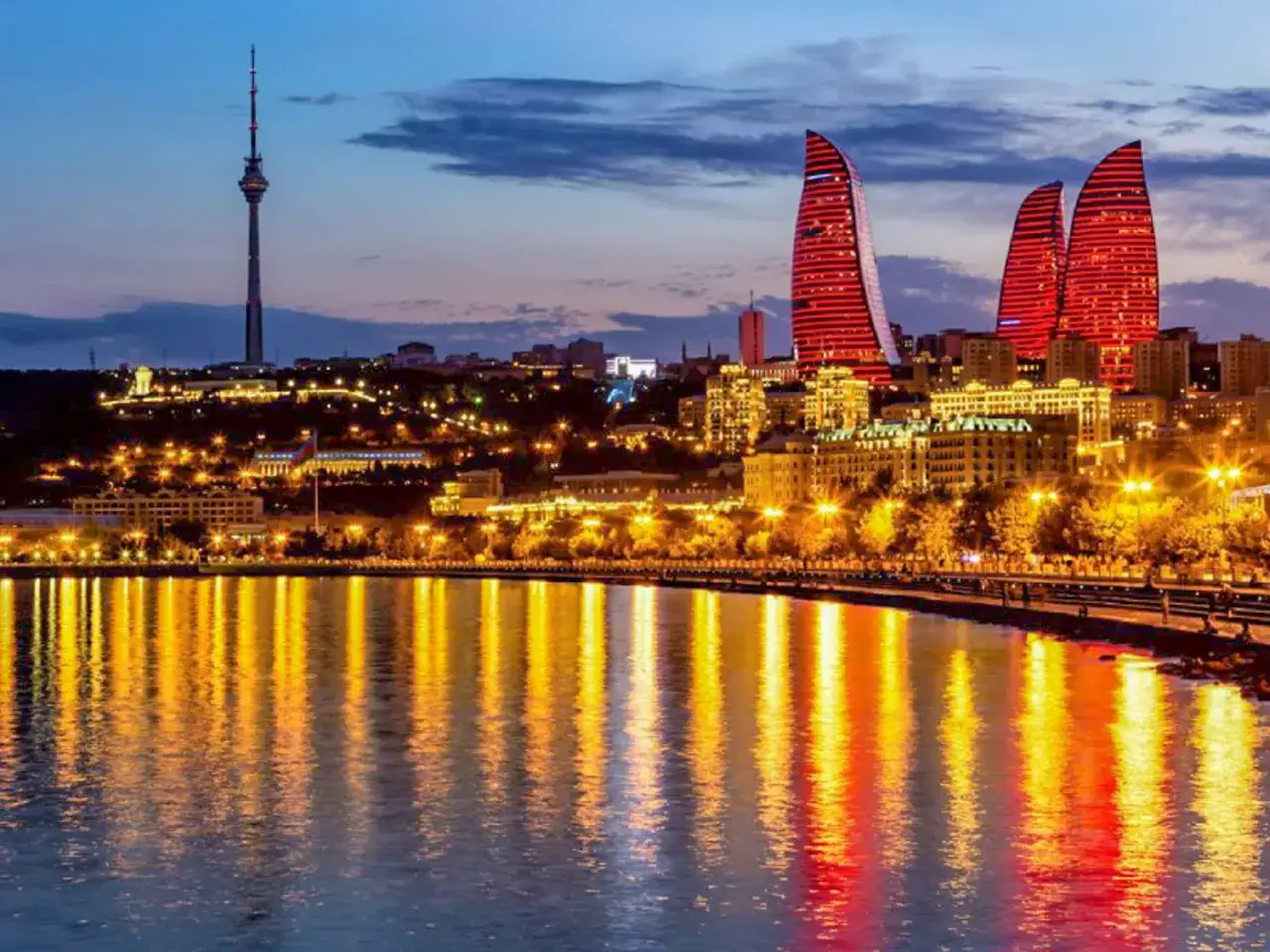 Baku nocą, z płomiennymi wieżowcami i odbiciami świateł w wodzie. Poznaj atrakcyjne ceny w Azerbejdżanie.