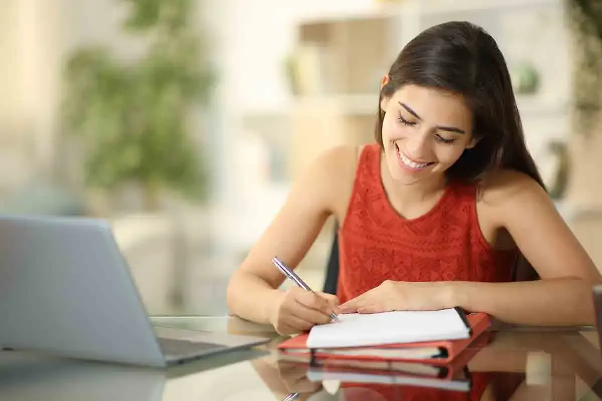 Ragazza sorridente scrive su quaderno, idee per cose da fare quando ti annoi per ragazze.