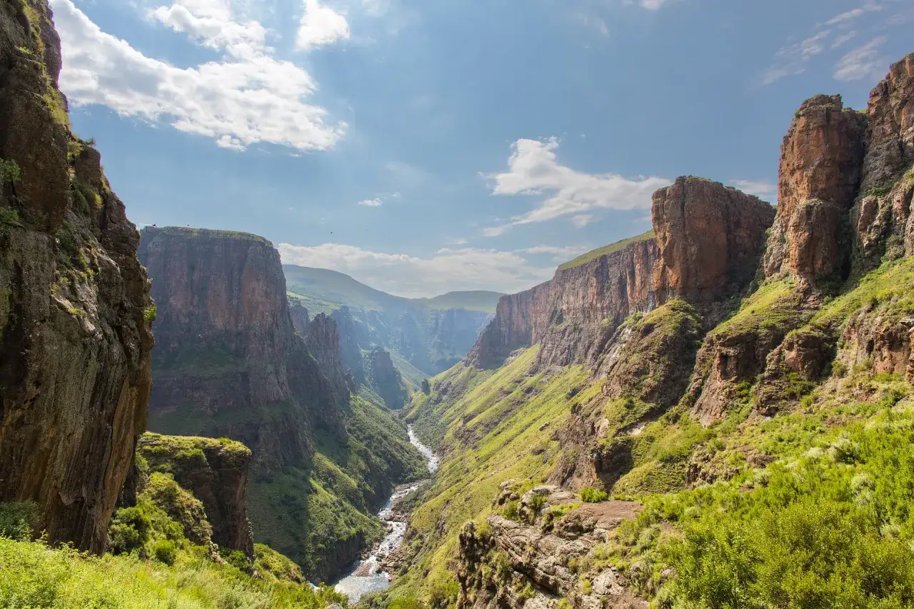 Głęboki kanion z rzeką i zielonymi zboczami, przypominający dziką metropolię Lesotho.