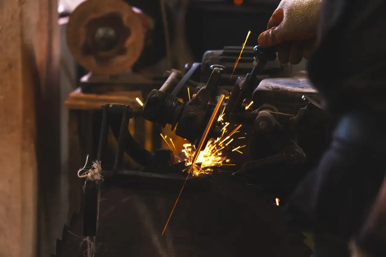 Scintille volano mentre una mano guantata lavora su una sega circolare, forse per affilare una radica di legno.