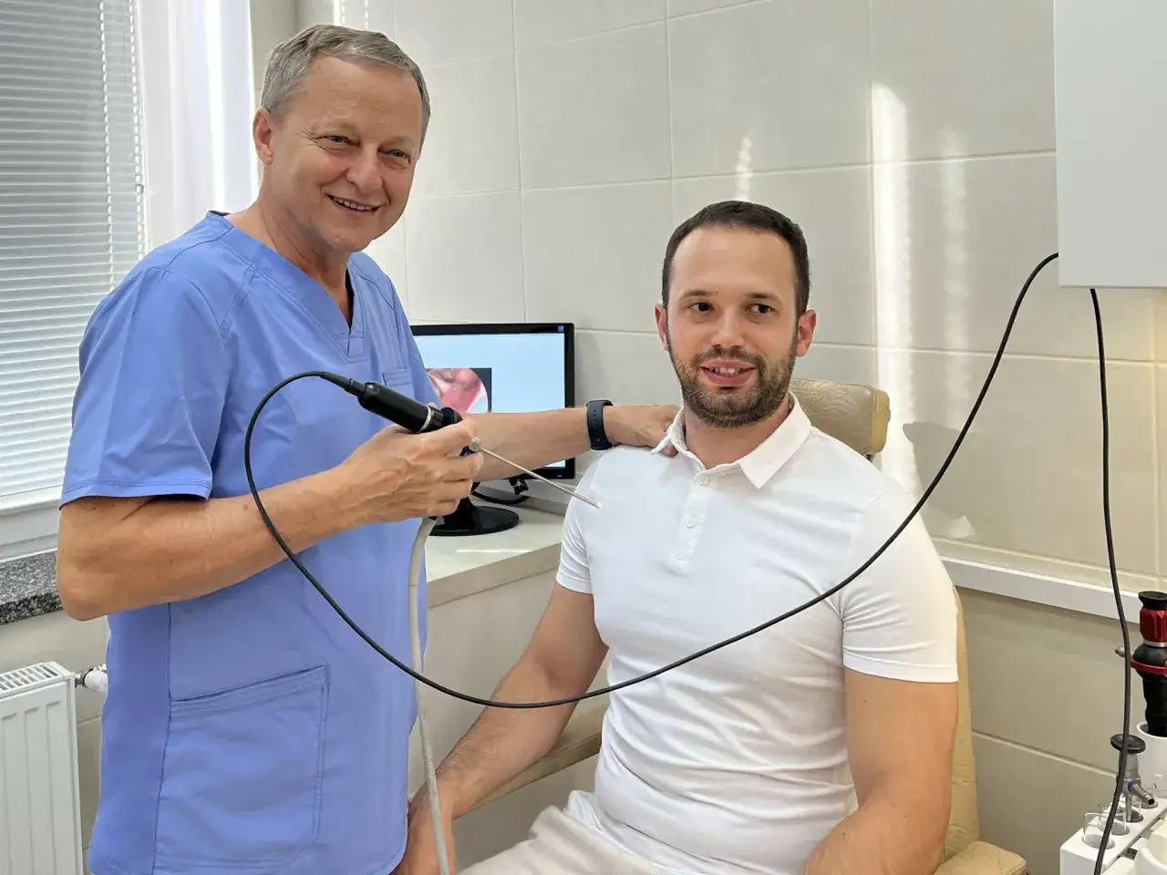 Lekarz w niebieskim fartuchu wykonuje fiberoskopię pacjentowi. Na ekranie widać obraz z endoskopu.