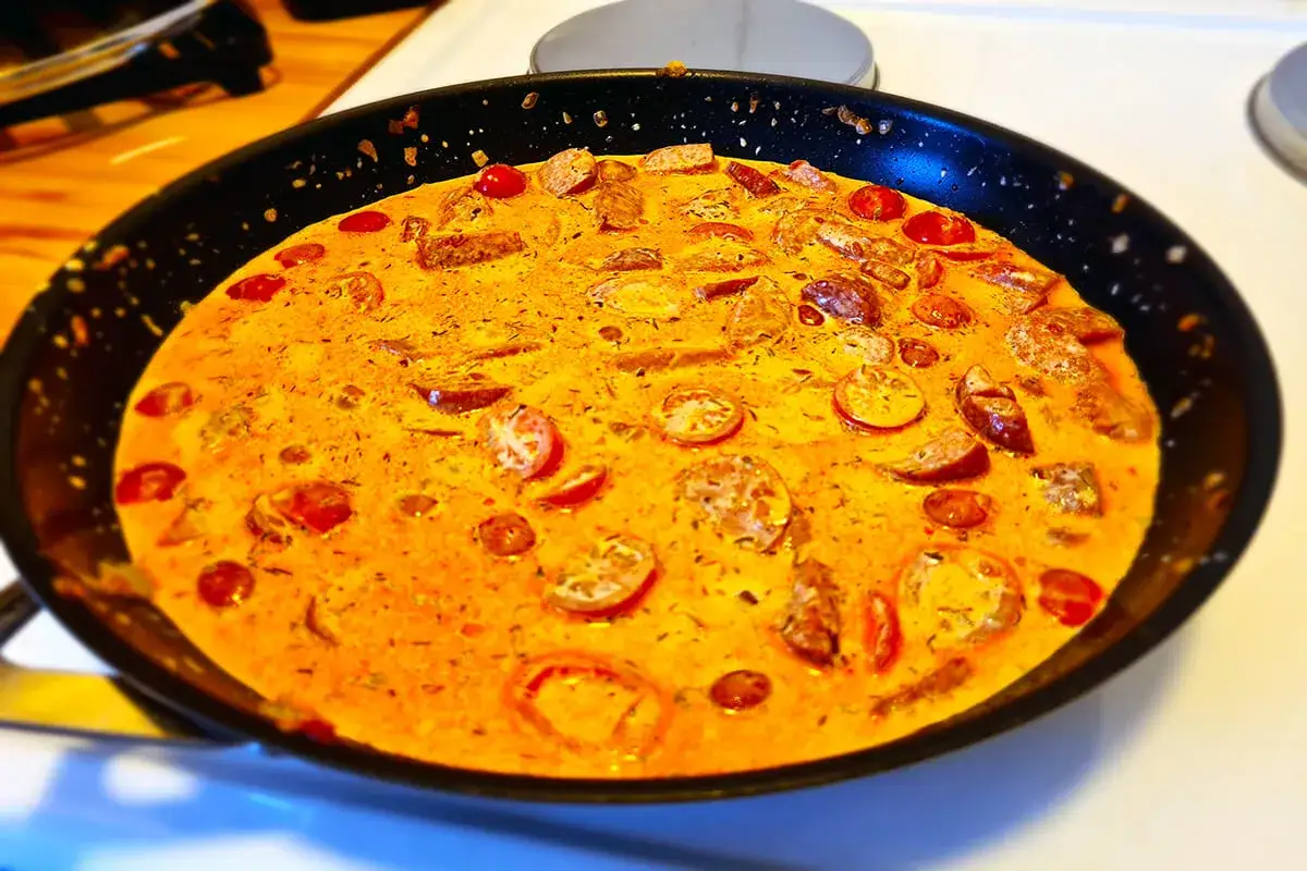 En panna med krämig korv stroganoff deluxe, full med korvbitar och körsbärstomater.