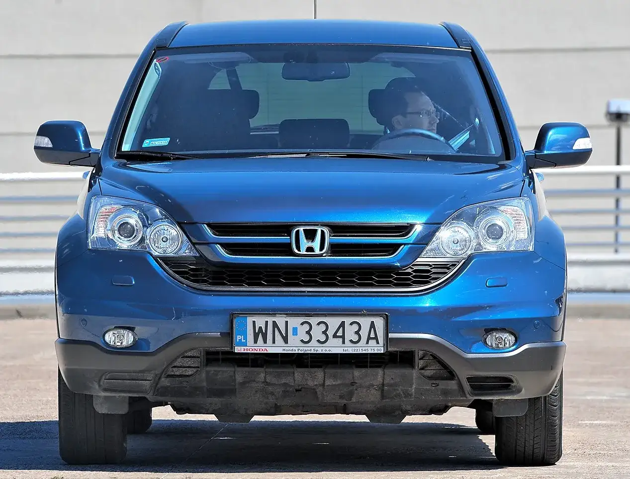 Niebieski SUV Honda CR-V z kierowcą. Czy to awd vs 4wd? Zbliżenie na przód auta z polskimi tablicami.