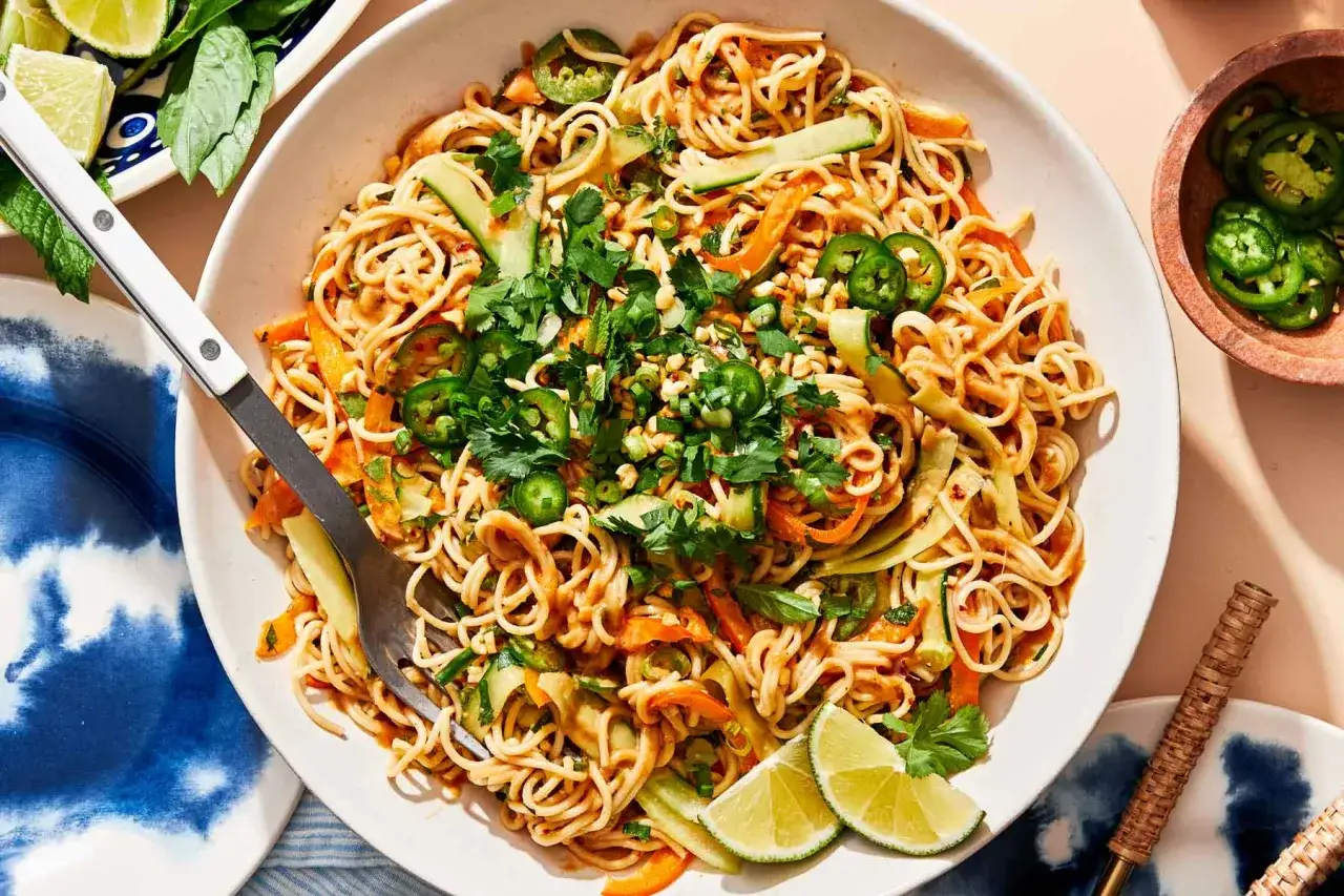 Ein köstlicher asia nudelsalat mit Gurke, Karotten, Jalapeños und Koriander, garniert mit Erdnüssen und Limettenspalten.