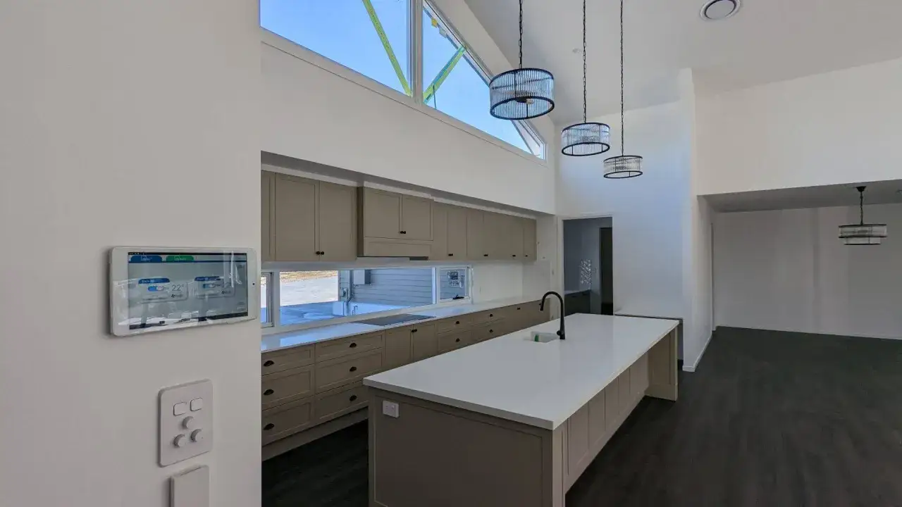 Panel t&aacute;ctil controla la climatizaci&oacute;n por conductos en una cocina moderna con isla central y gabinetes color arena.