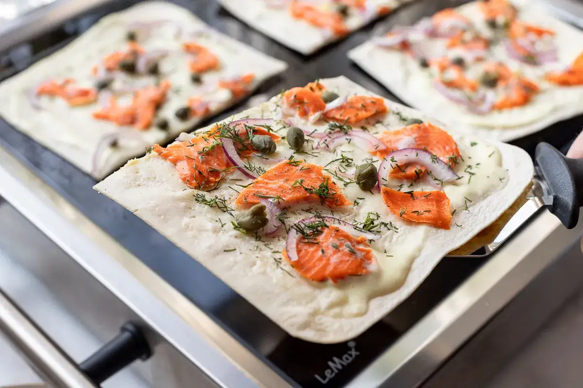 Flammkuchen mit Lachs, roten Zwiebeln und Kapern wird auf einem Grill zubereitet.