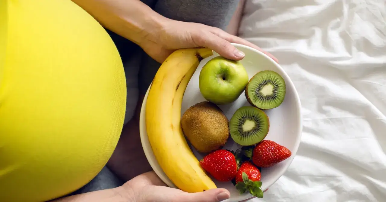 Talerz z owocami dla ciężarnej: banan, jabłko, kiwi, truskawki. Pamiętaj, czego nie jeść w ciąży, by dbać o zdrowie.