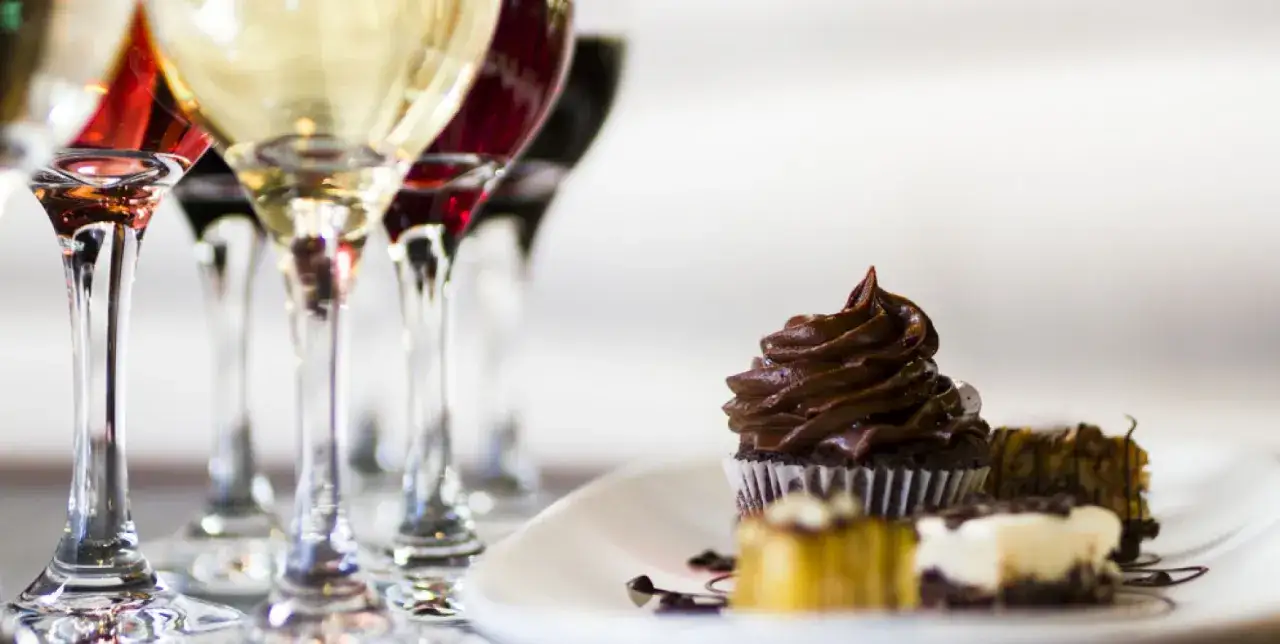 Calici di vino rosso e bianco accanto a un piattino con cupcake al cioccolato e altri dolcetti, perfetti per accompagnare vini da dessert.