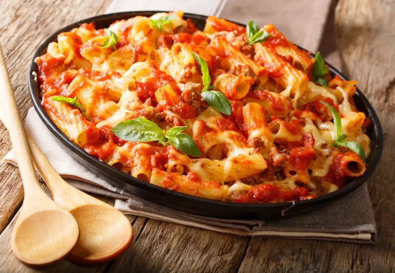 Macarrones con carne picada, cubiertos de salsa de tomate y queso fundido, decorados con hojas de albahaca fresca. ¡Un plato casero irresistible!