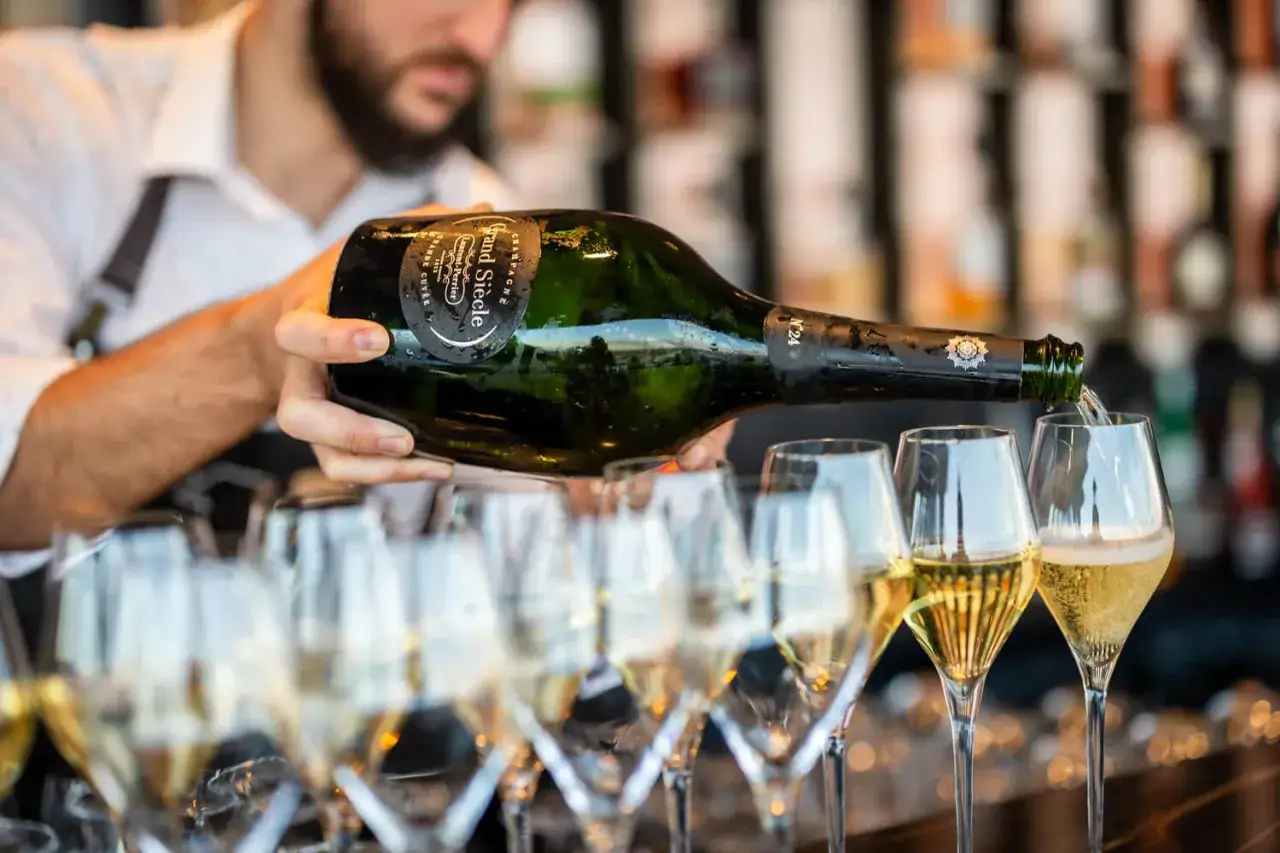 Un serveur verse du champagne Grand Siècle, un type de champagne prestigieux, dans une rangée de flûtes.
