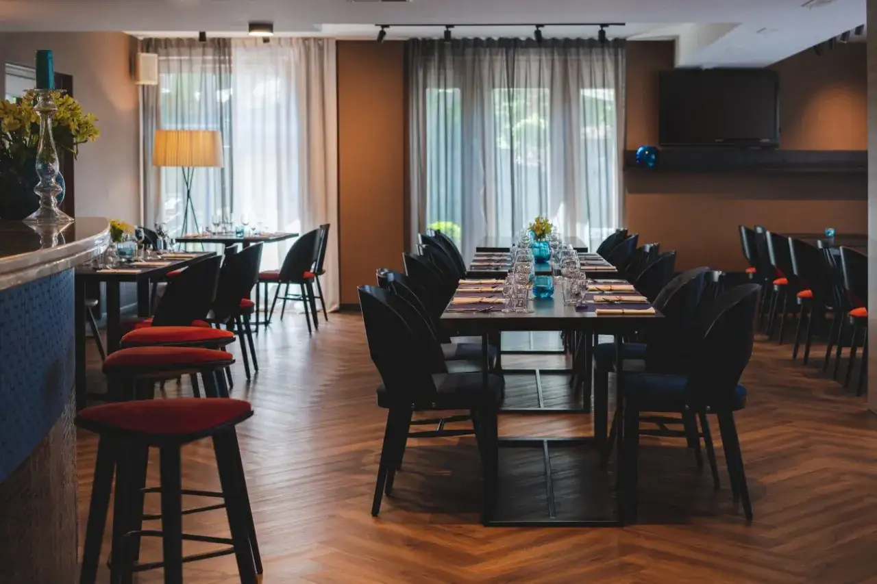 Elegancka restauracja w hotelu Perła Kraków. Stoły nakryte do kolacji, krzesła w ciemnych barwach, czerwone hokery przy barze.