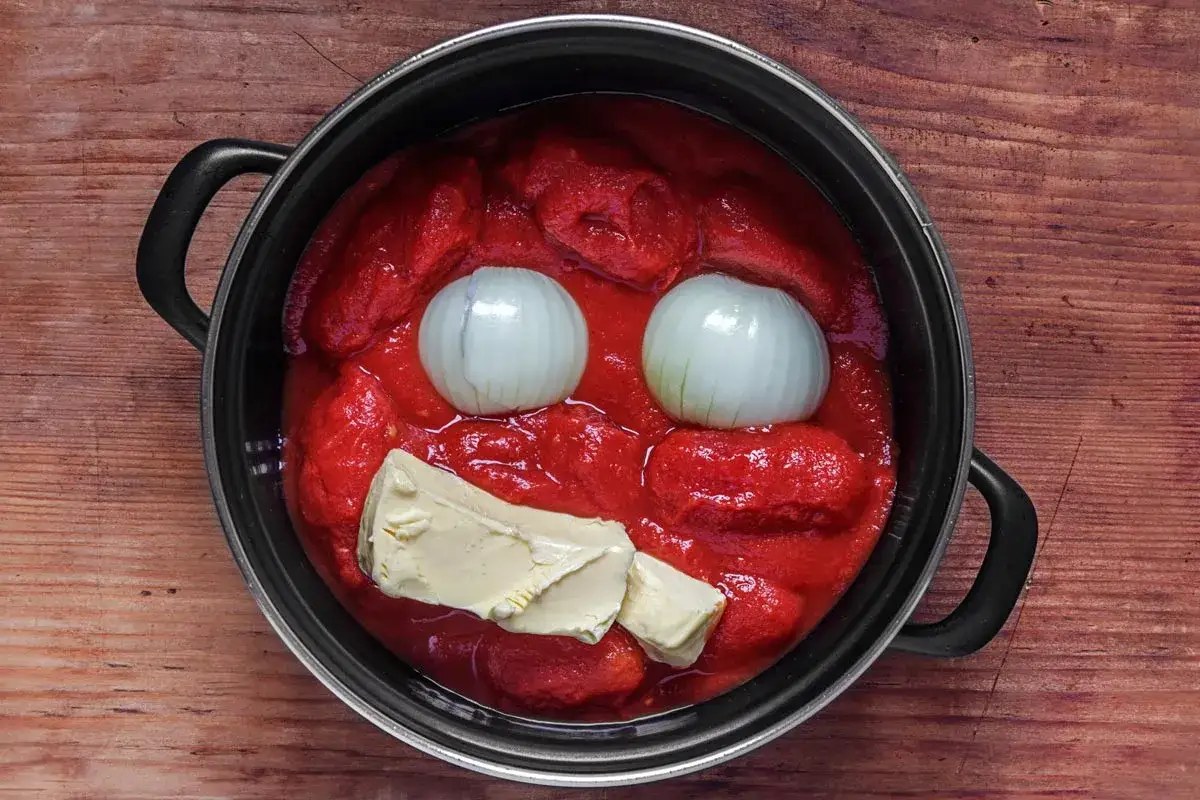 Ein Topf mit italienischer Tomatensauce, zwei Zwiebeln als Augen und Butter als Mund, sieht aus wie ein lachendes Gesicht.