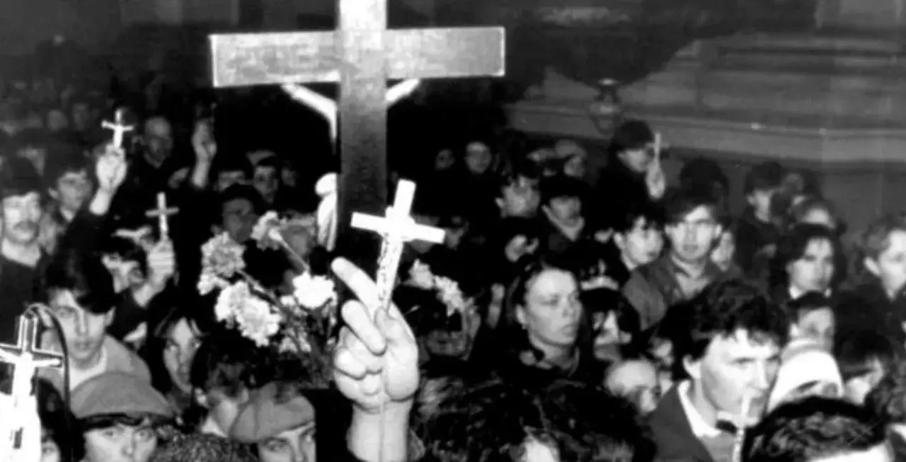 Tłum ludzi z krzyżami w rękach, słychać głośny chant po polsku. Widać kwiaty i emocje na twarzach.