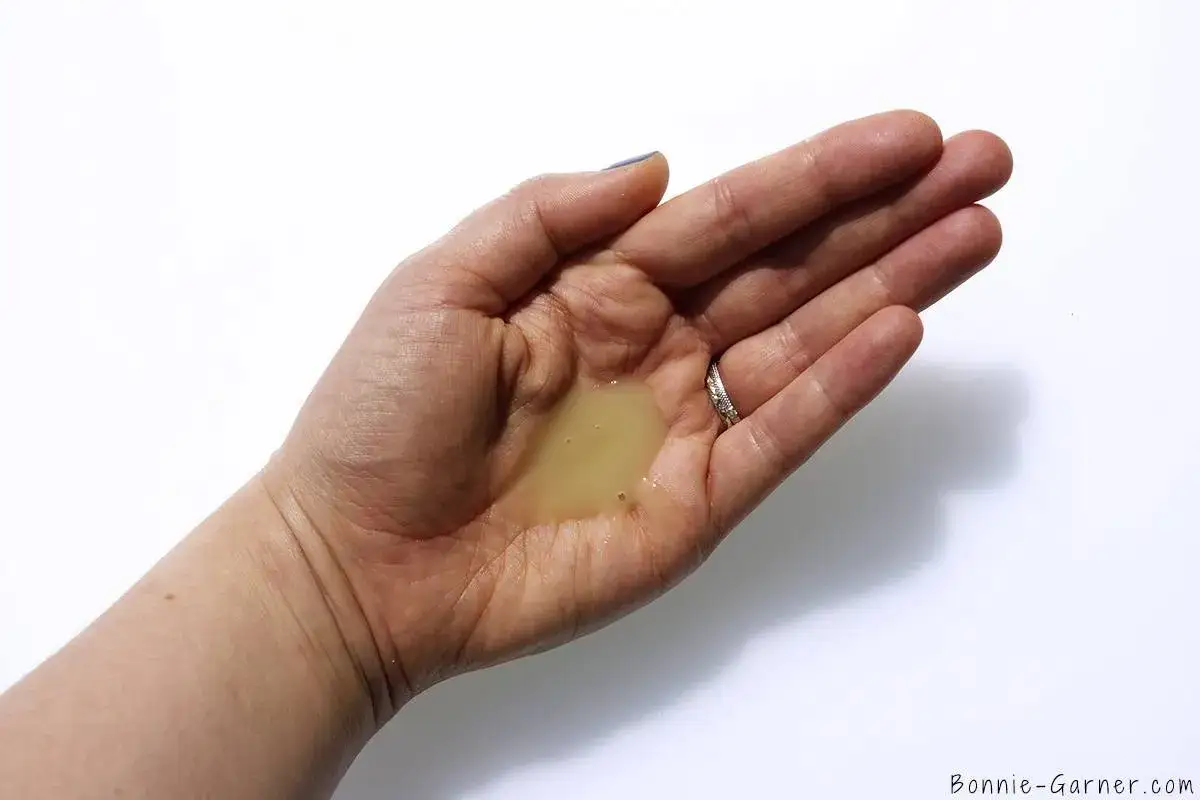 Une main ouverte tient une petite quantité de shampoing jaune, posant la question : combien de shampoing par lavage pour un résultat optimal ?