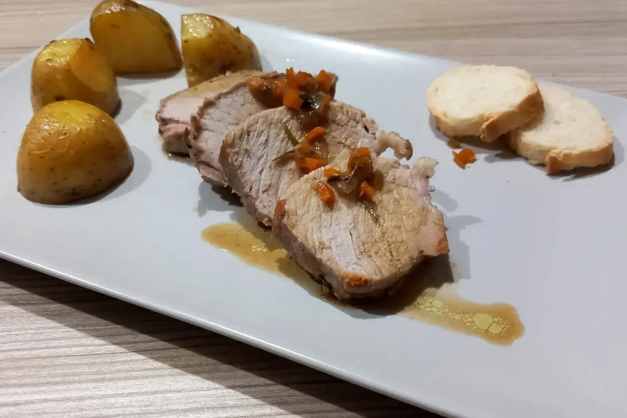 Arista di maiale affettata con patate arrosto e fette di pane.